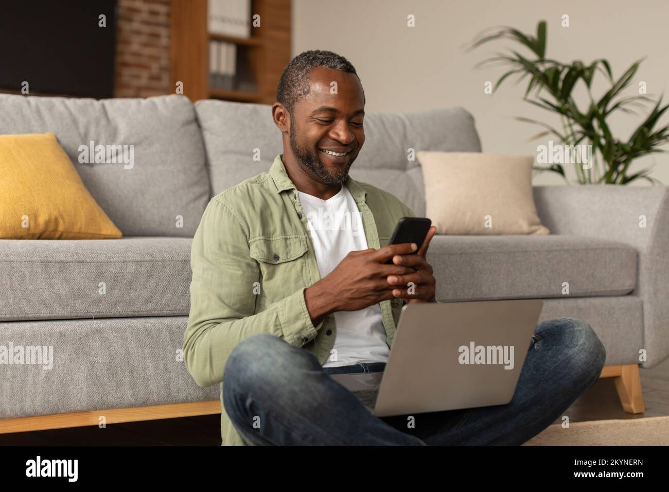 App for work, business remote. Happy middle aged african american male with laptop typing on phone Stock Photo