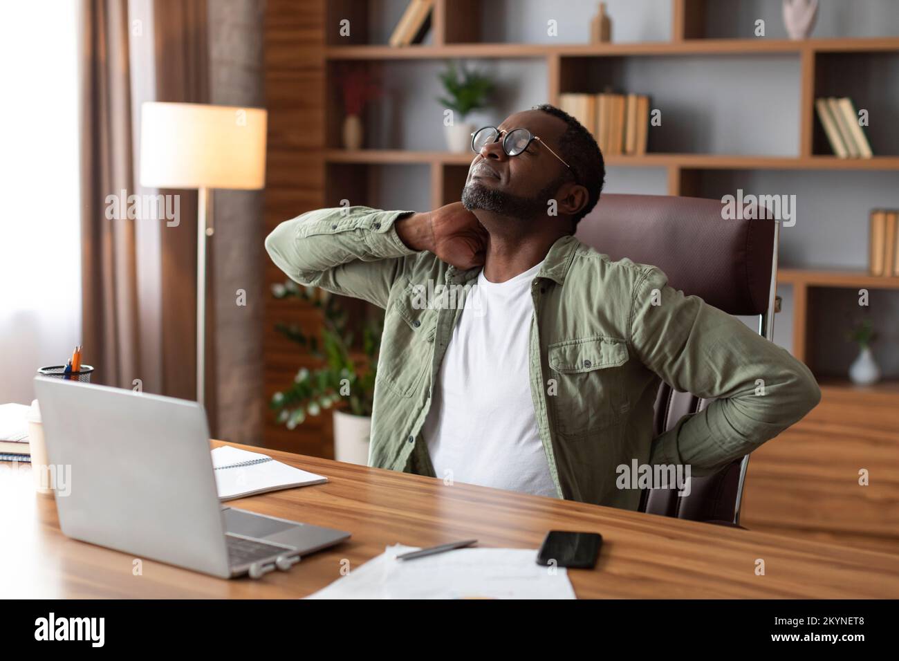 Unhappy despair middle aged african american businessman in glasses suffering from back pain at table Stock Photo