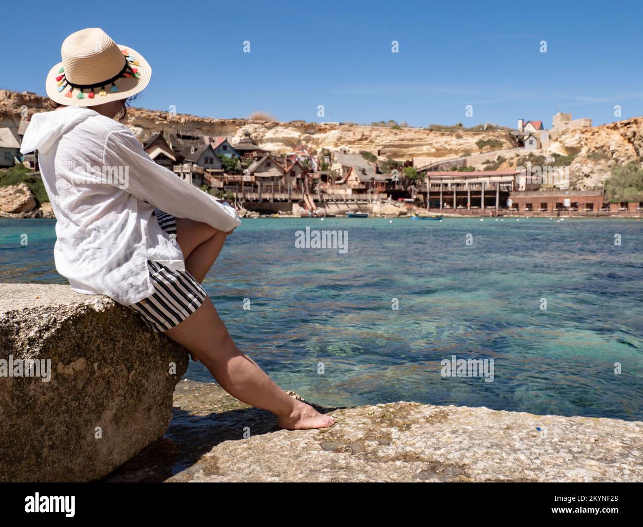 Mellieha, Malta - May 2021: A woman in a white shirt with a straw hat in front of the village of Popeye in Malta. Europe Stock Photo