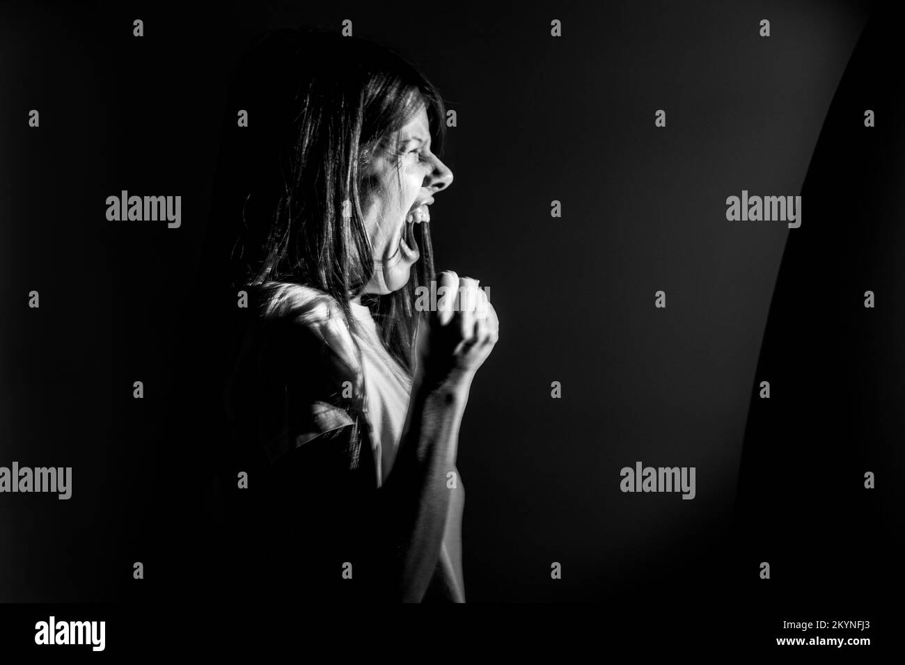 The girl screams in the dark from anger and rage, pain and scream Stock Photo
