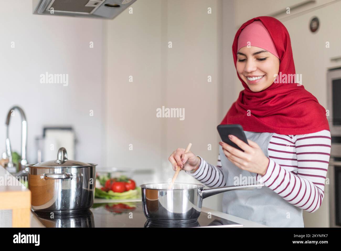 Muslim lady cooking at home, reading culinary blog on smartphone Stock Photo