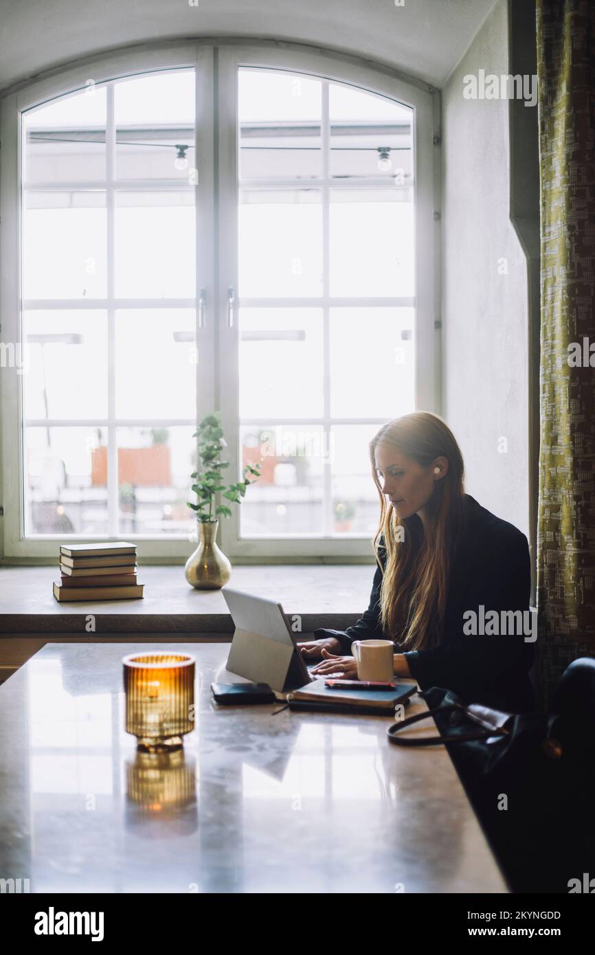 Female freelancer using laptop while sitting at table in restaurant Stock Photo