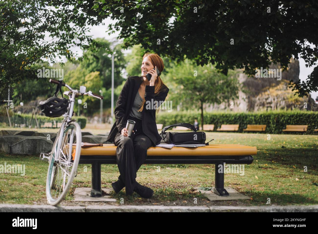 Happy businesswoman talking on mobile phone while sitting by bicycle at park Stock Photo