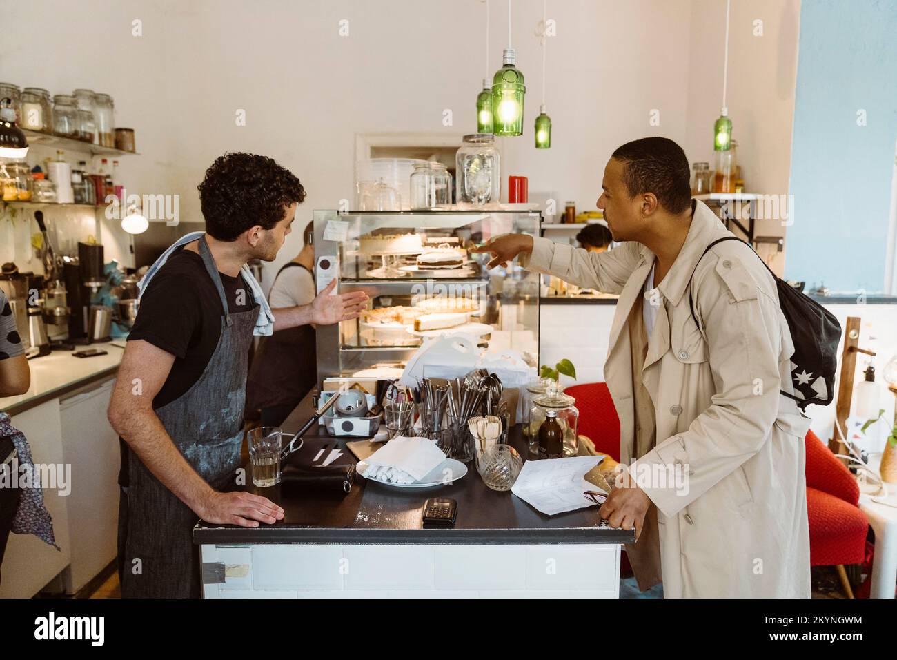 Side view of male cafe owner suggesting food to customer at counter Stock Photo