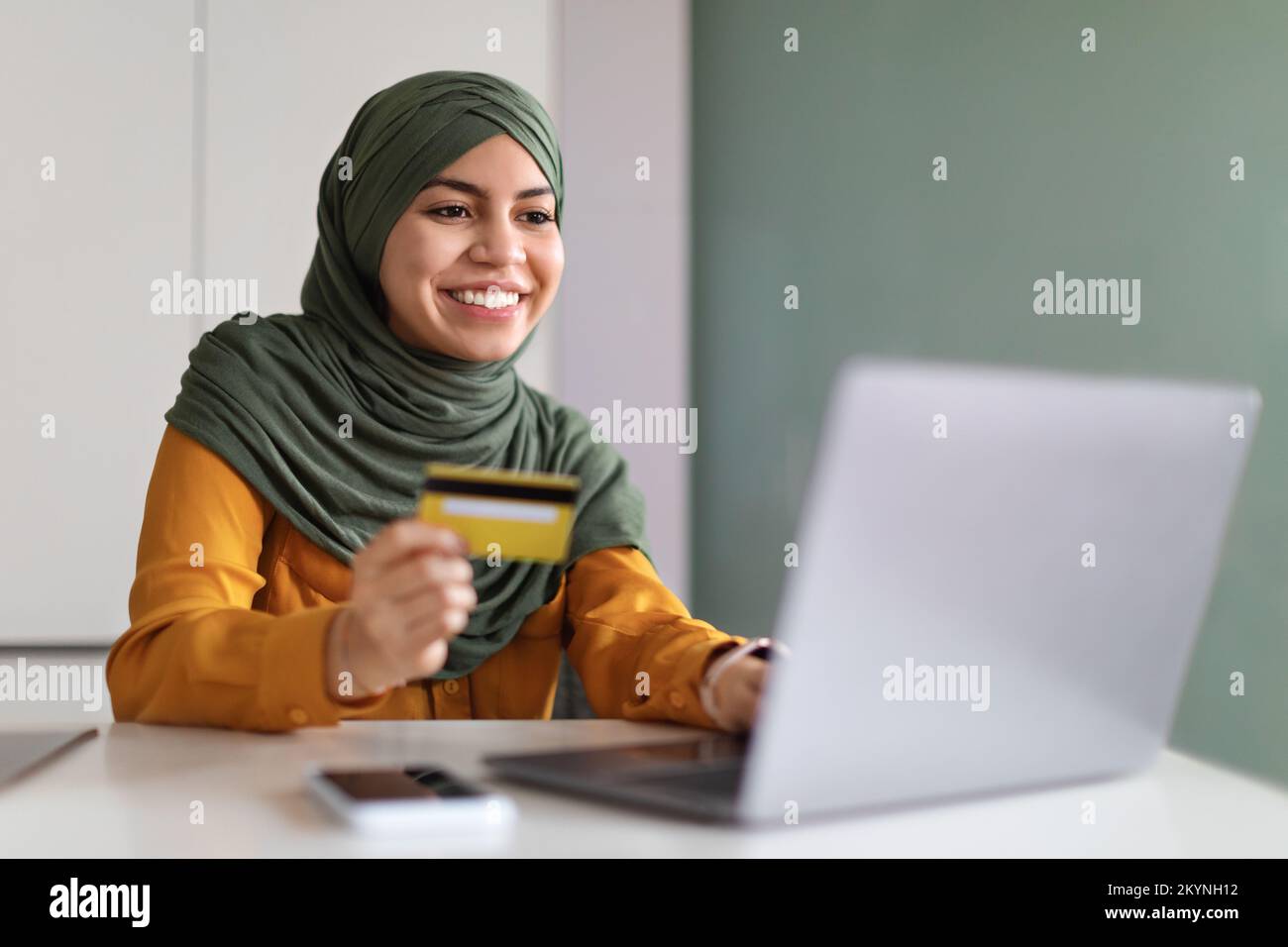 Online Payments. Smiling Muslim Woman In Hijab Using Laptop And Credit Card Stock Photo