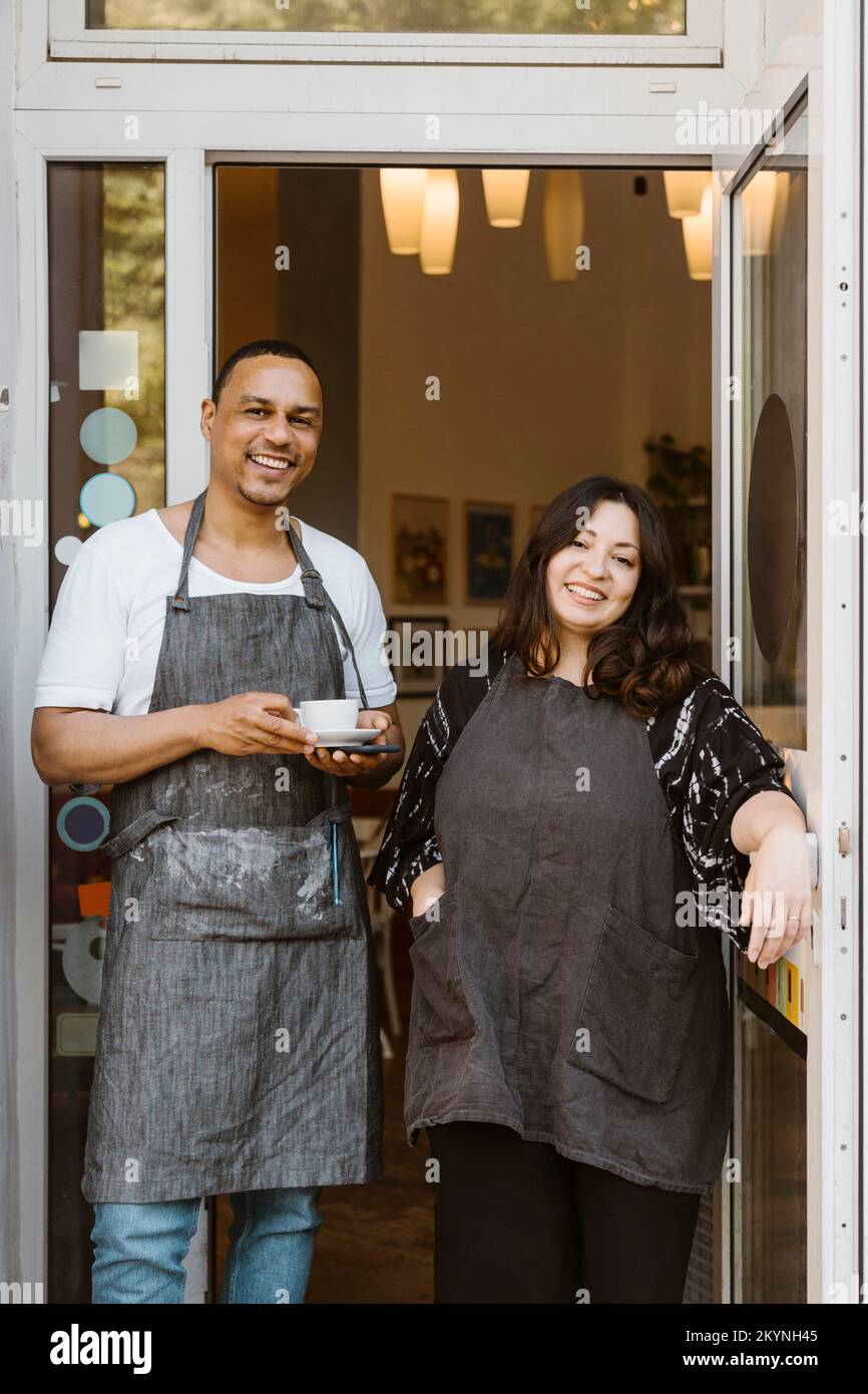 Portrait of happy multiracial male and female cafe owners standing at doorway Stock Photo