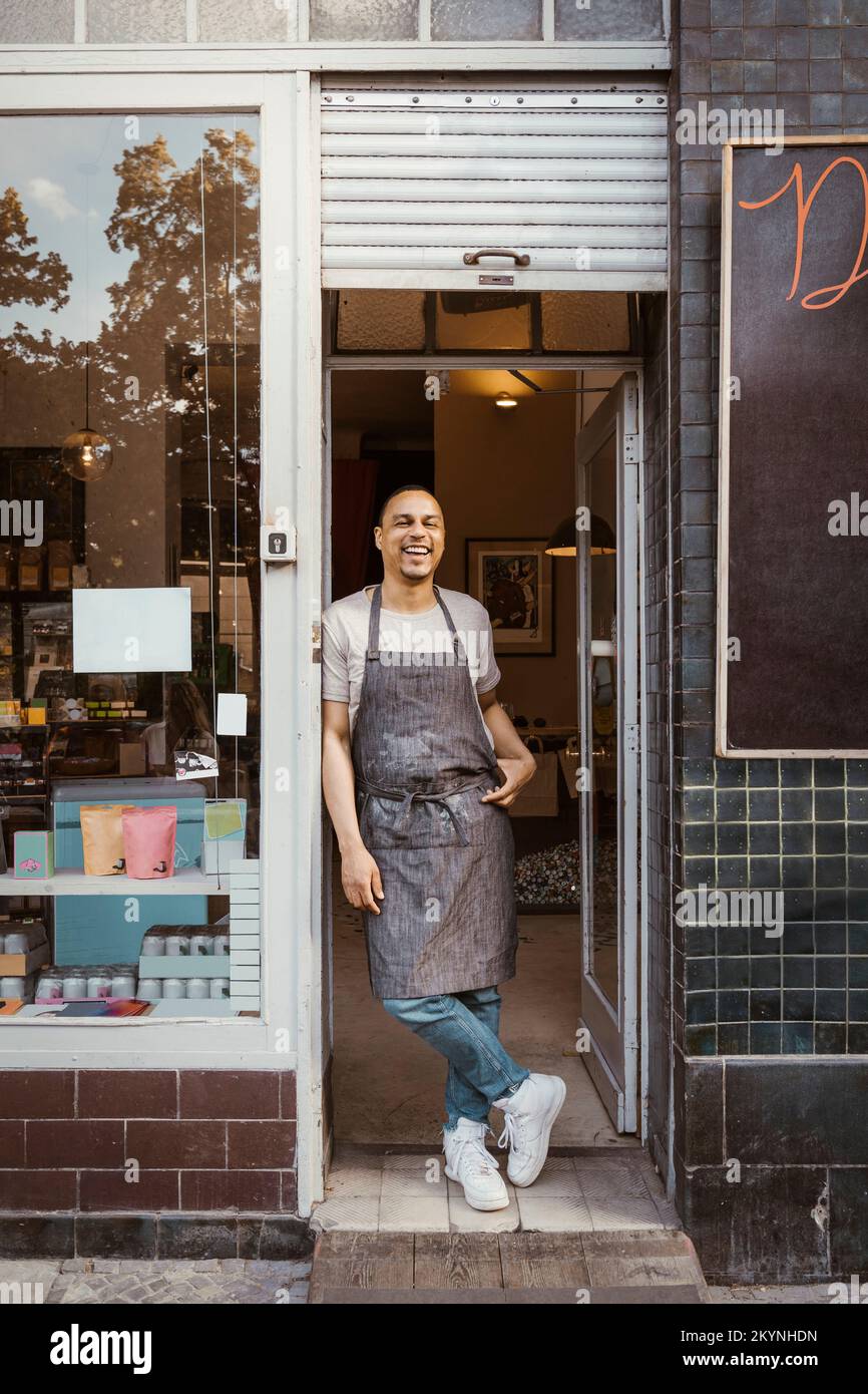 Happy male deli owner wearing apron leaning on doorway Stock Photo Alamy