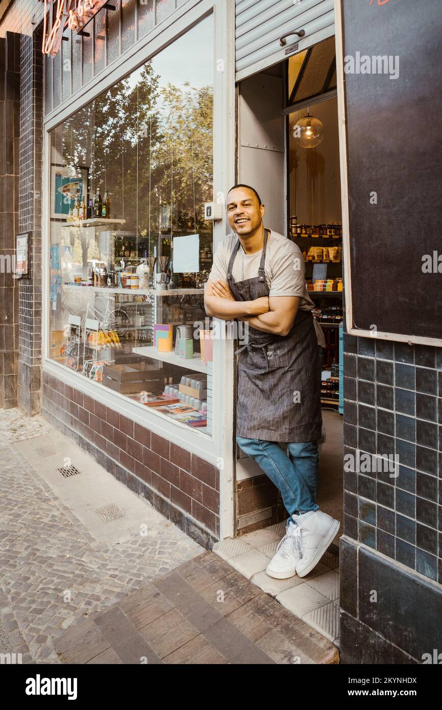 Smiling male owner with arms crossed leaning at shop doorway Stock Photo