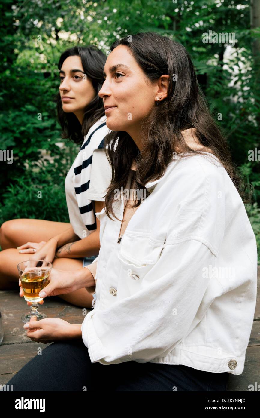 Smiling woman holding drink glass while sitting with female friend at party Stock Photo