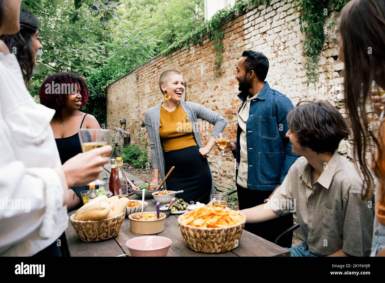 Young woman with hand on hip talking to friends during social gathering in back yard Stock Photo