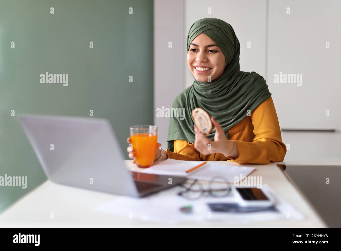 Young Muslim Woman Eating Snacks In Front Of Laptop At Home Stock Photo