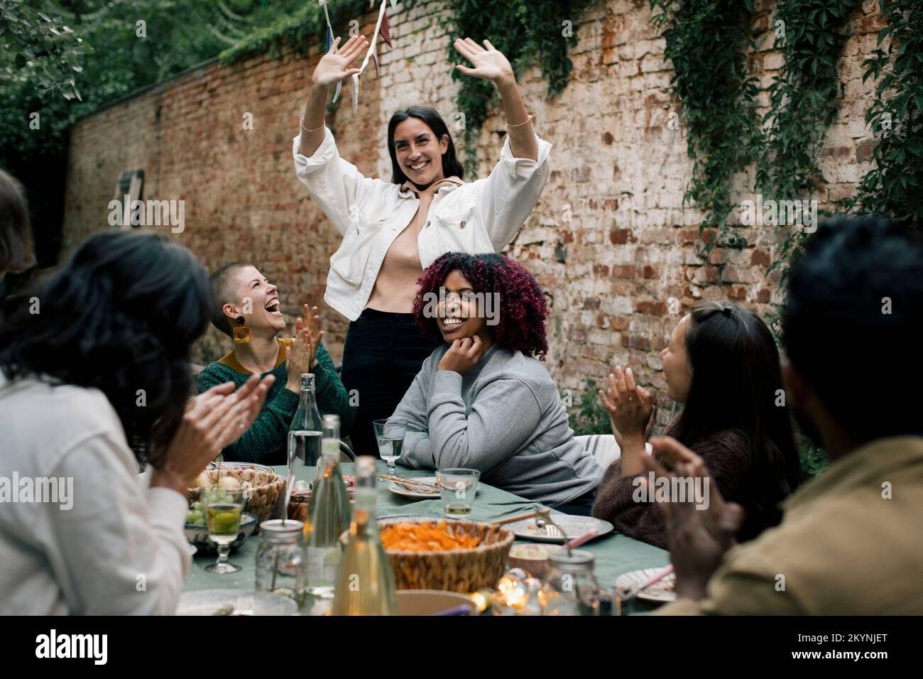 Smiling woman gesturing while enjoying with friends during dinner party in back yard Stock Photo