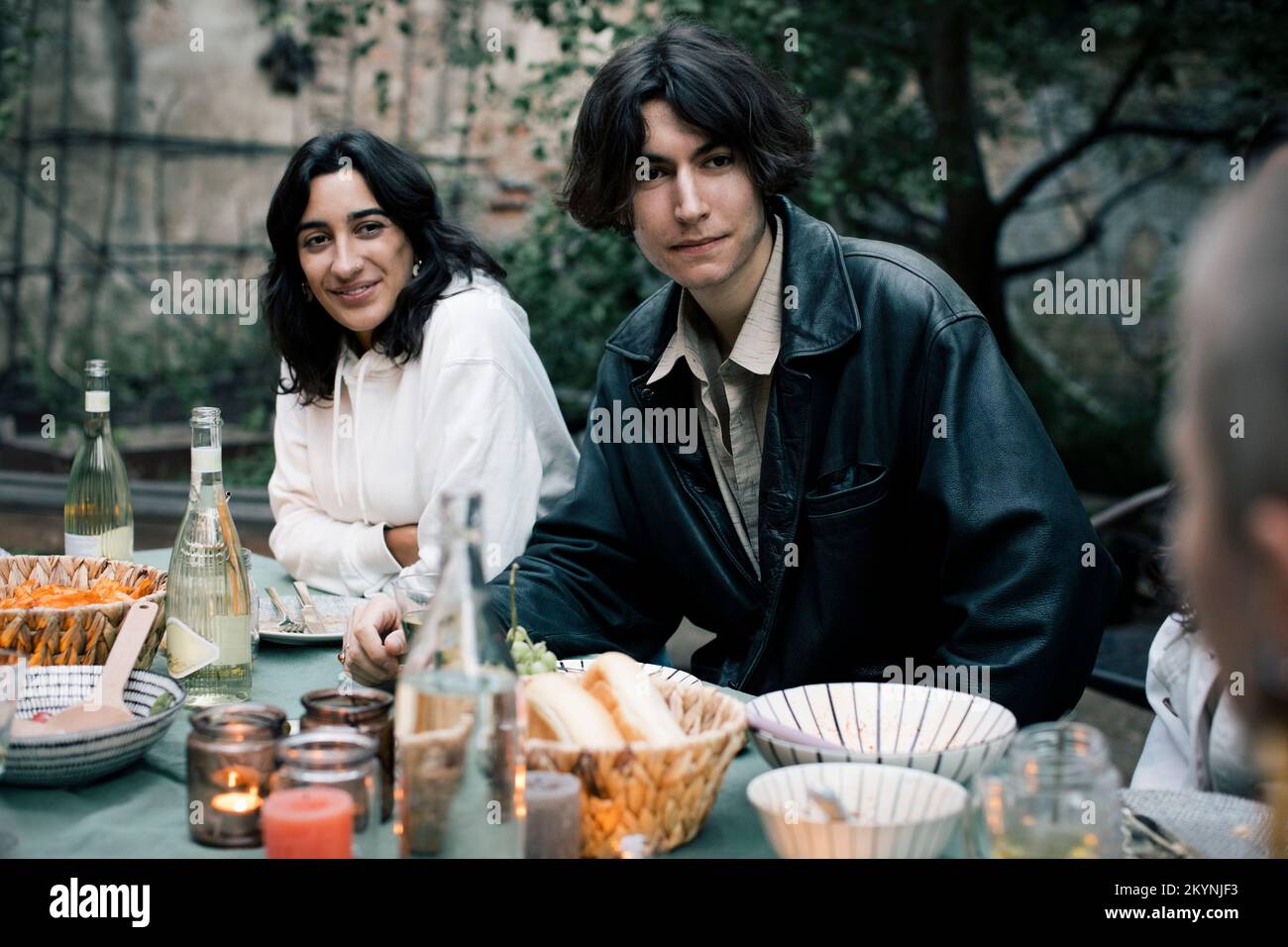 Man wearing leather jacket sitting with female friend during dinner party Stock Photo