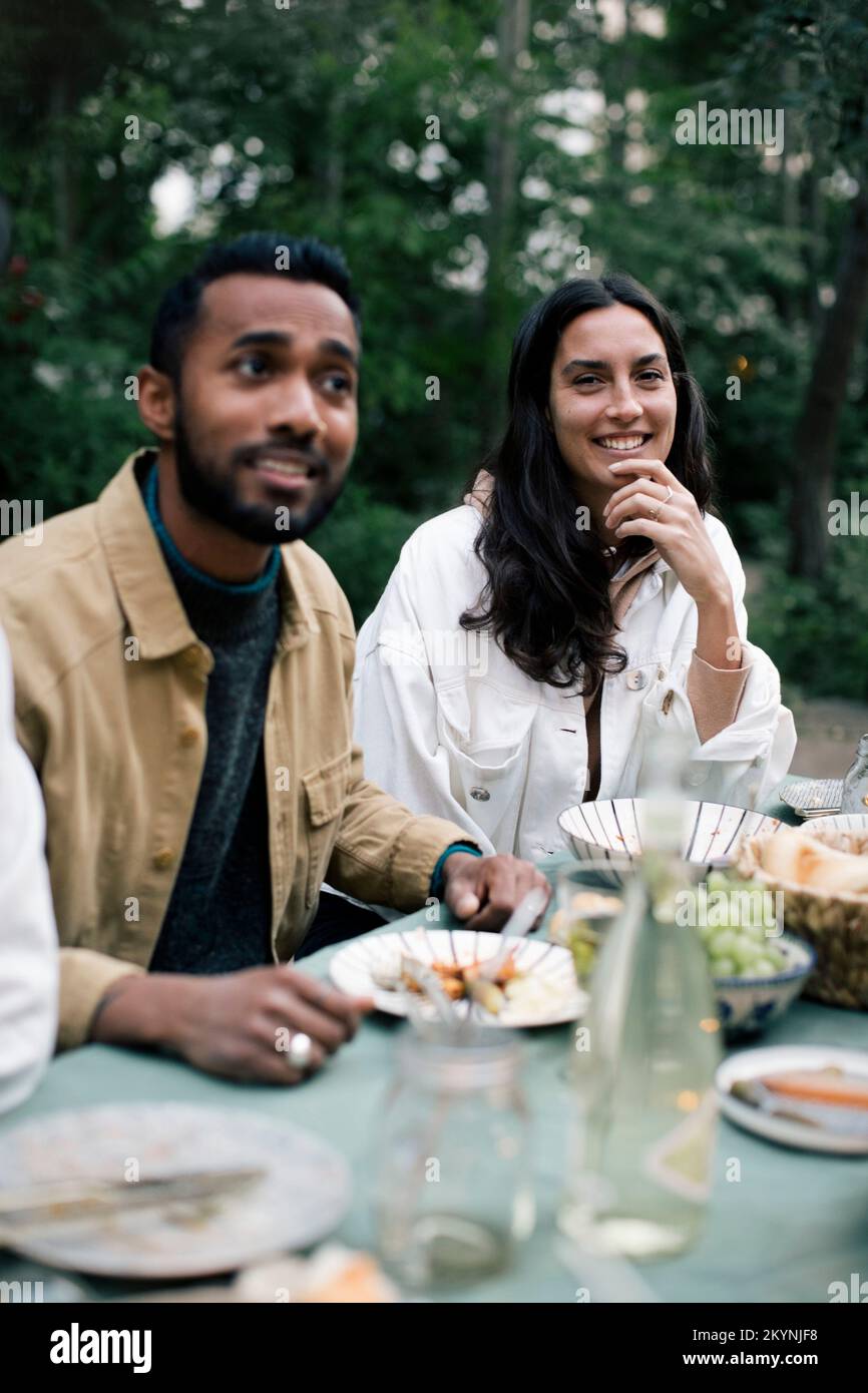 Smiling woman with hand on chin sitting by male friend at dinner party Stock Photo