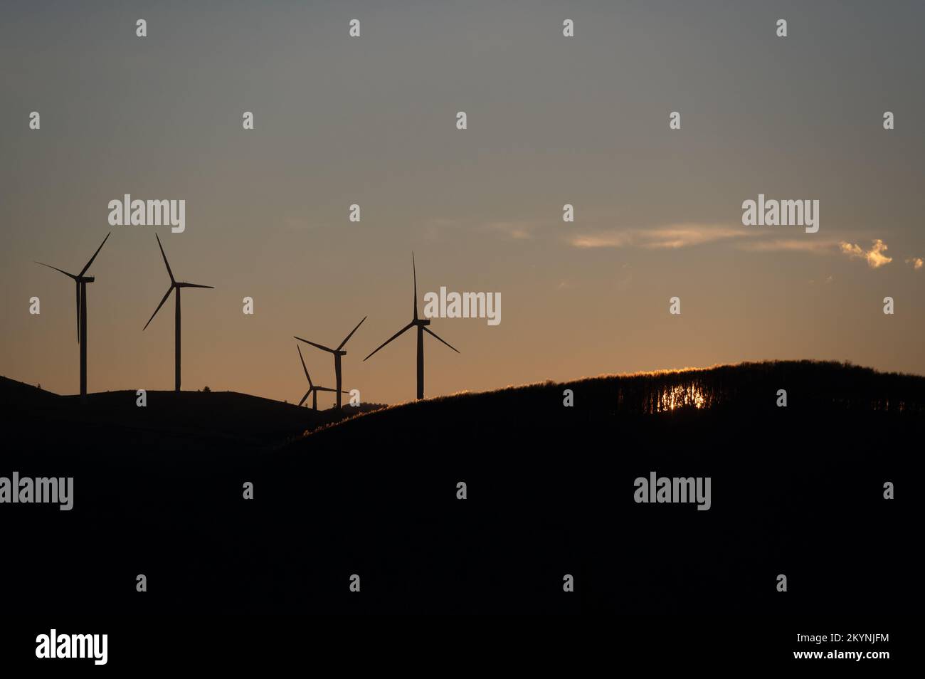 Wind turbines, a source of renewable energy, are silhouetted on a hilltop at sunrise. Stock Photo