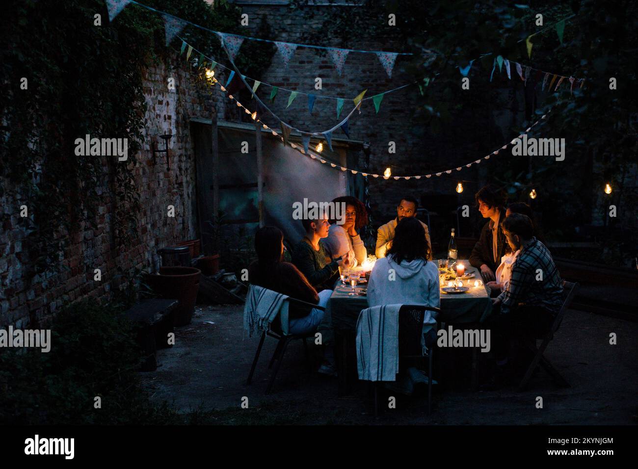 Multiracial friends during dinner party in illuminated back yard Stock Photo