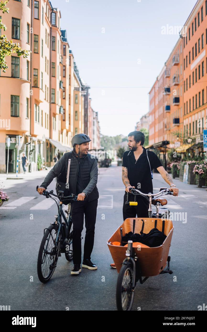 Male business colleagues with bicycles talking while standing on road Stock Photo