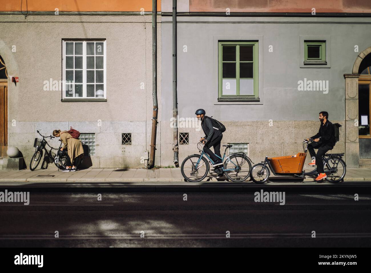 Male commuters riding bikes on road against building during sunny day Stock Photo