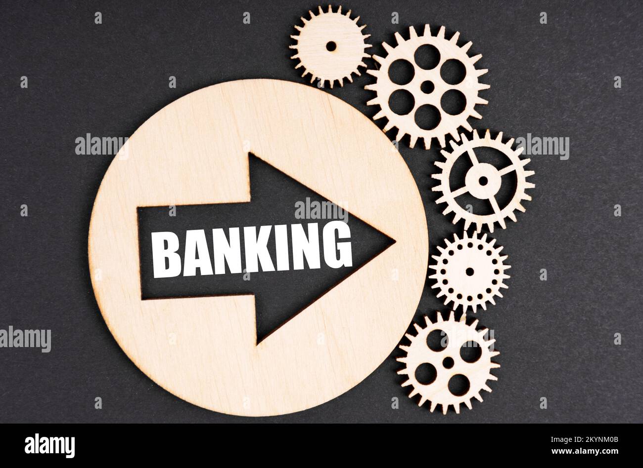 Business and finance concept. On a black background, there are wooden gears and a circle inside which there is an arrow with the inscription - Banking Stock Photo