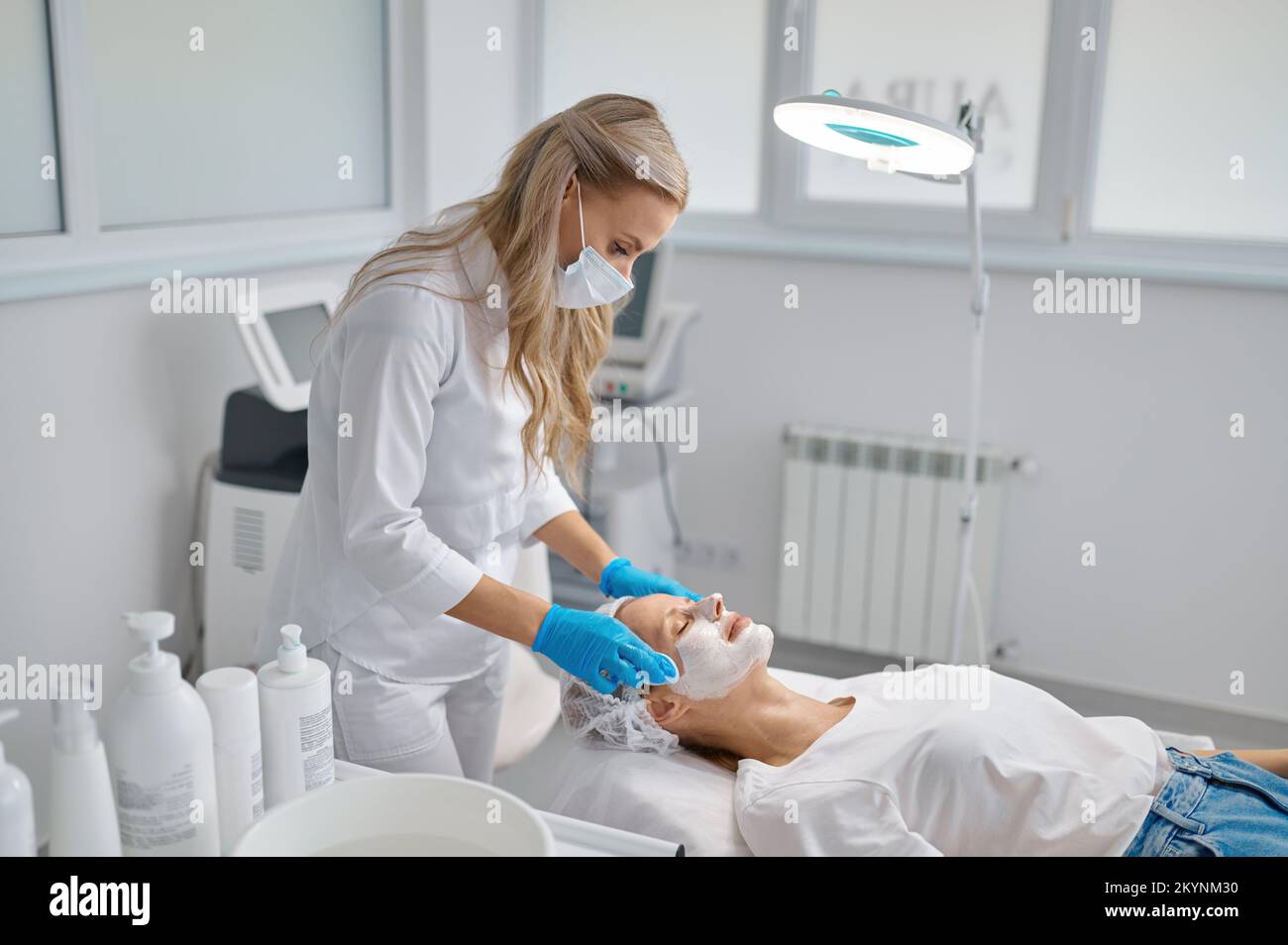 Beautician washes woman face using cotton pads to remove face mask Stock Photo