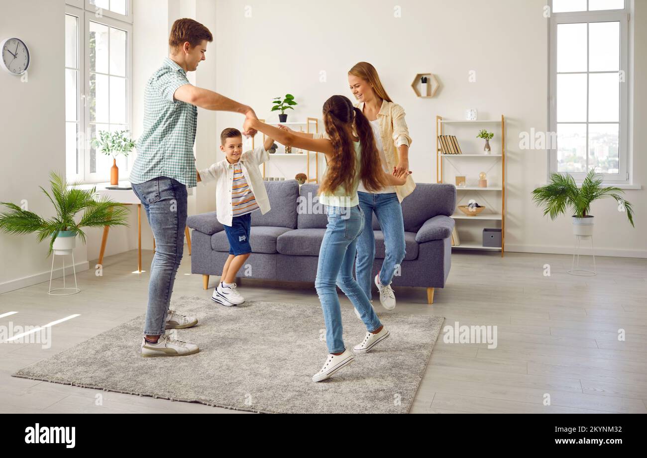 Happy family mom, dad, daughter and son playing leading a round dance at home in living room. Stock Photo