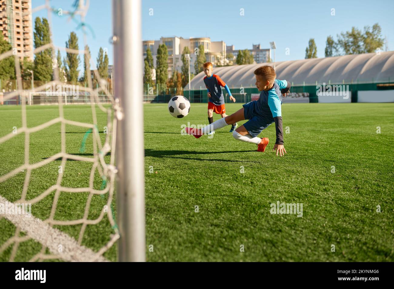 Boy football player kicking ball into gate on sports field Stock Photo