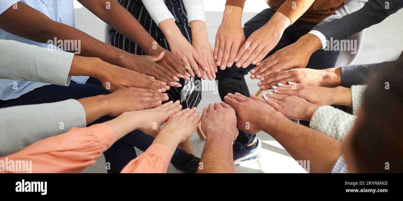Multiracial men and women put their hands together in circle as symbol of cooperation and unity. Stock Photo