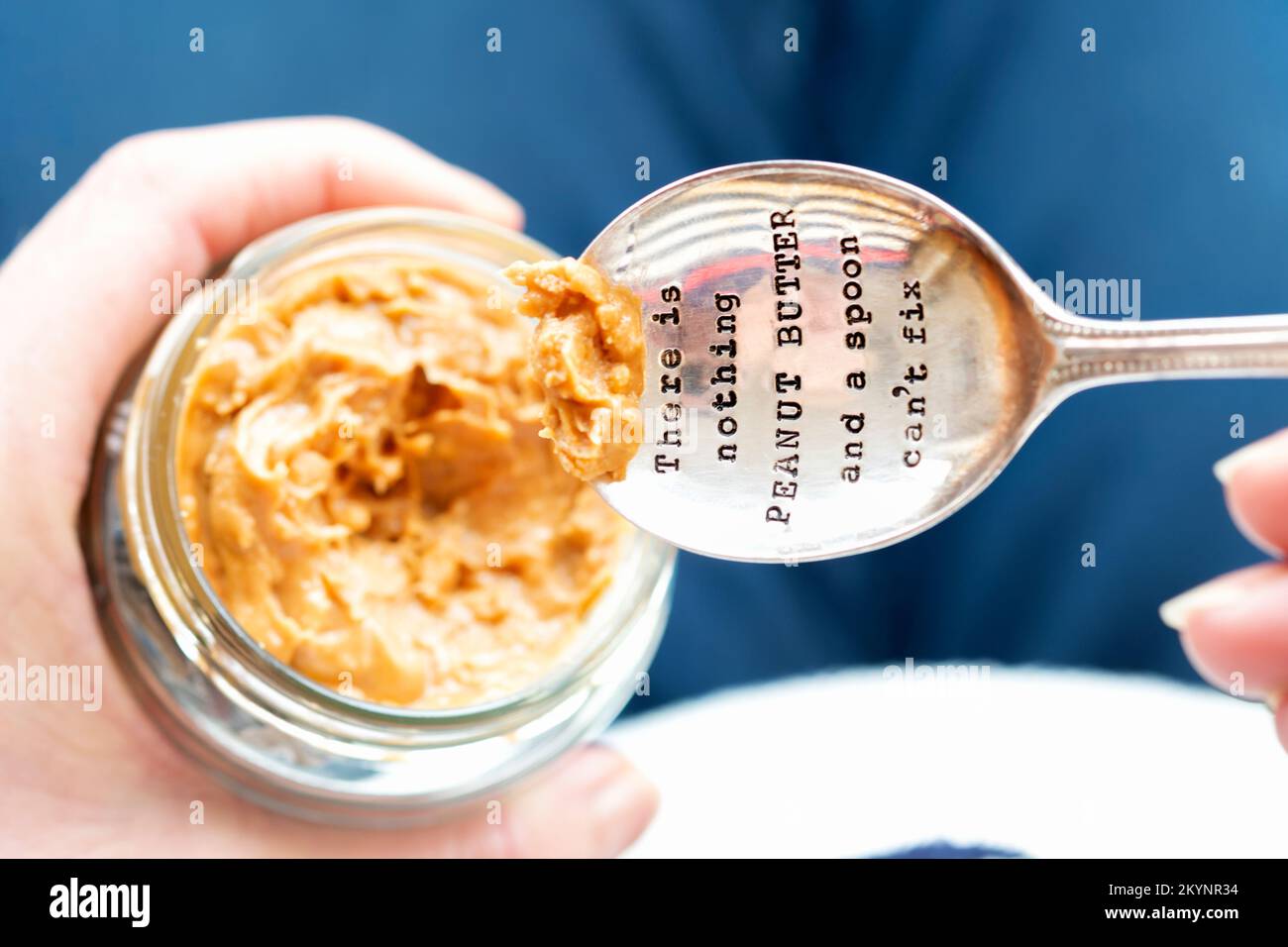 A silver spoon stamped with a message. There is nothing peanut butter and a spoon can’t fix. The spoon is dipped into a jar of peanut butter. Stock Photo