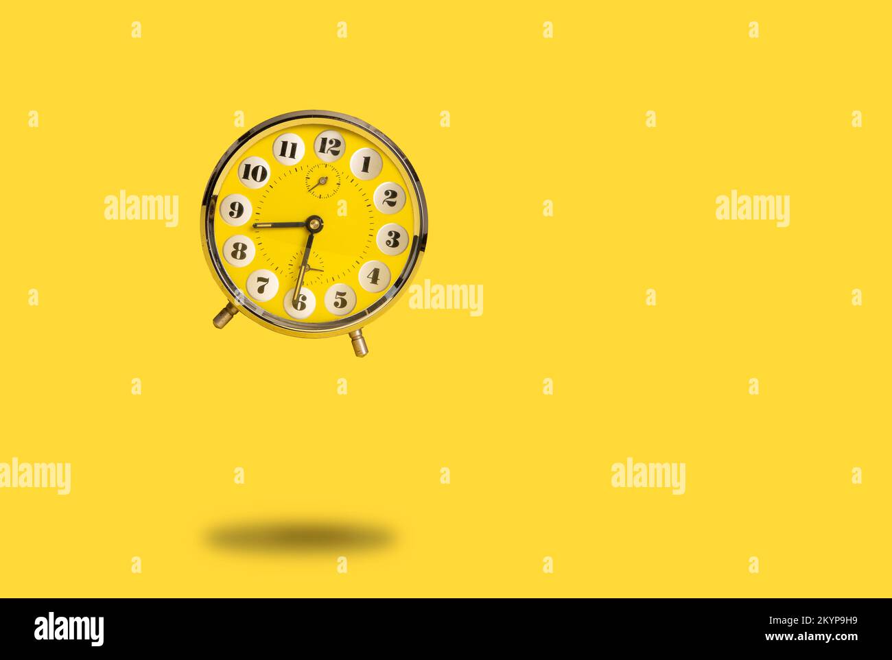 Round yellow alarm clock flying above the ground as a concept for time