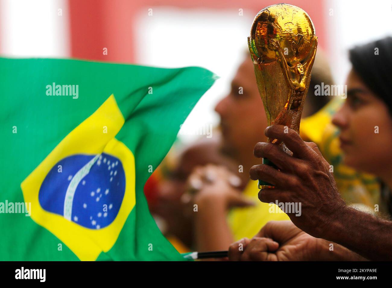 Fifa World Cup trophy replica close up detail and brazilian flag. Soccer fan hand holding award in celebration, supporting national football team Stock Photo