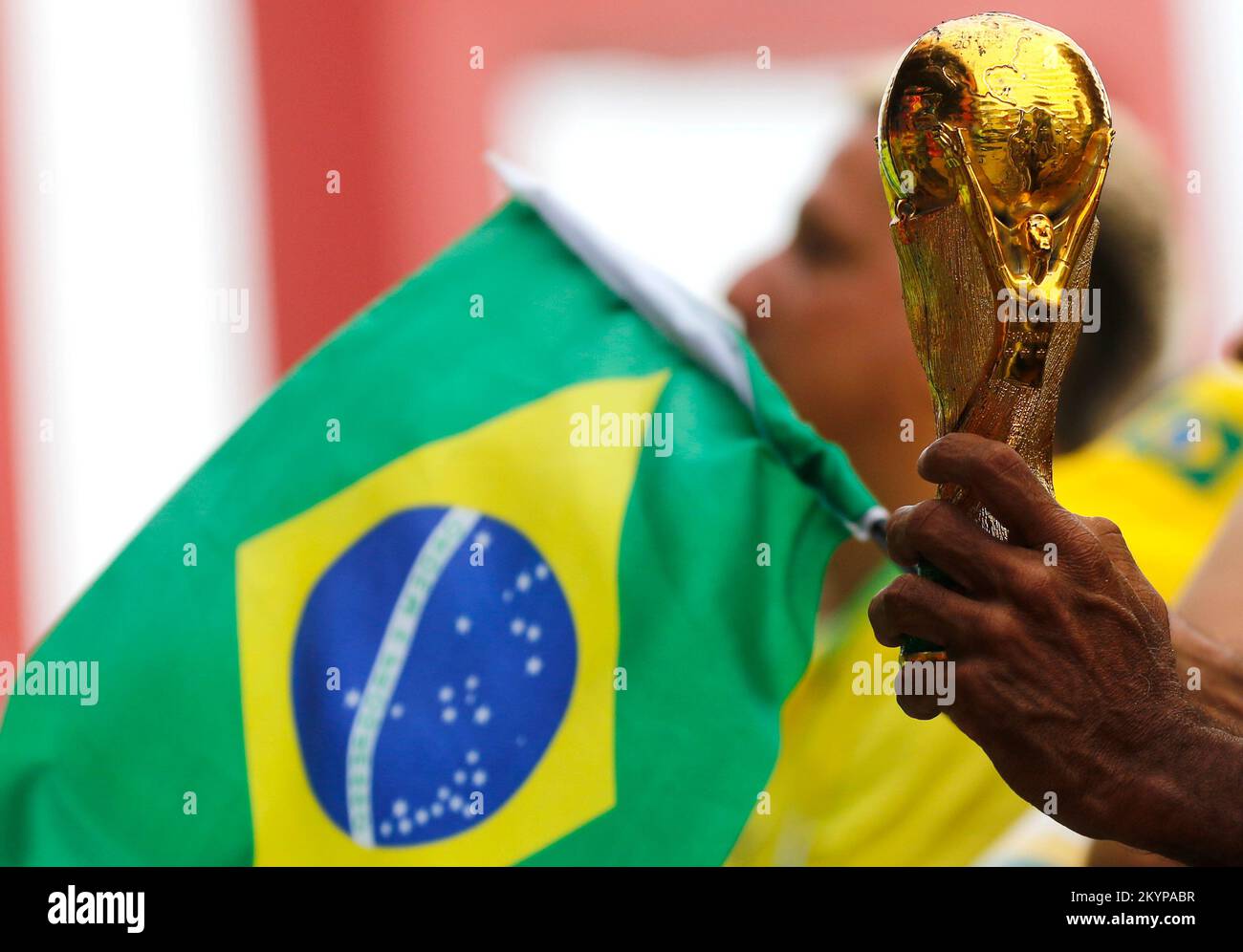 Fifa World Cup trophy replica close up detail and brazilian flag. Soccer fan hand holding award in celebration, supporting national football team Stock Photo