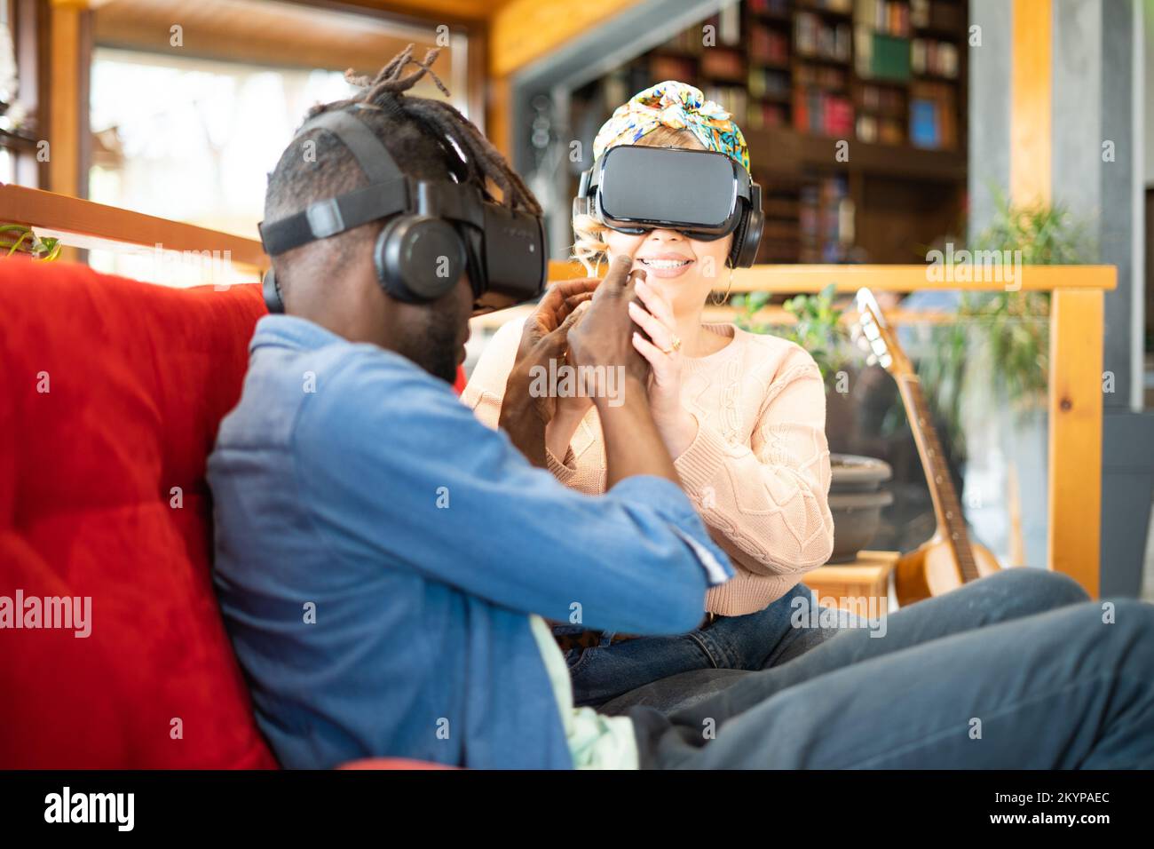 Multiethnic friends couple meeting himself in 3d reality on the red couch - New wearable technology concept Stock Photo