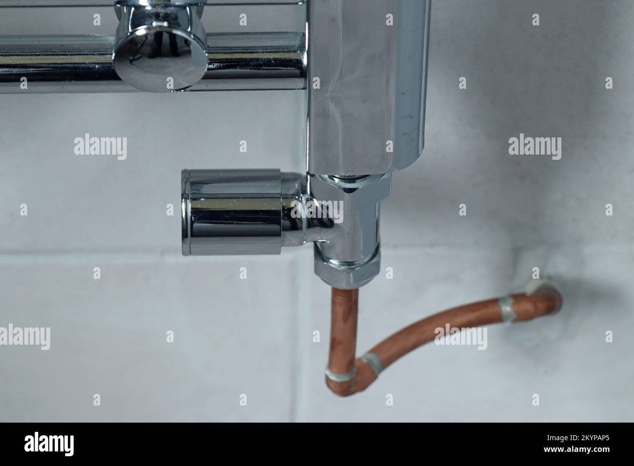 Closeup of the lockshield valve on a chrome radiator in a grey tiled
