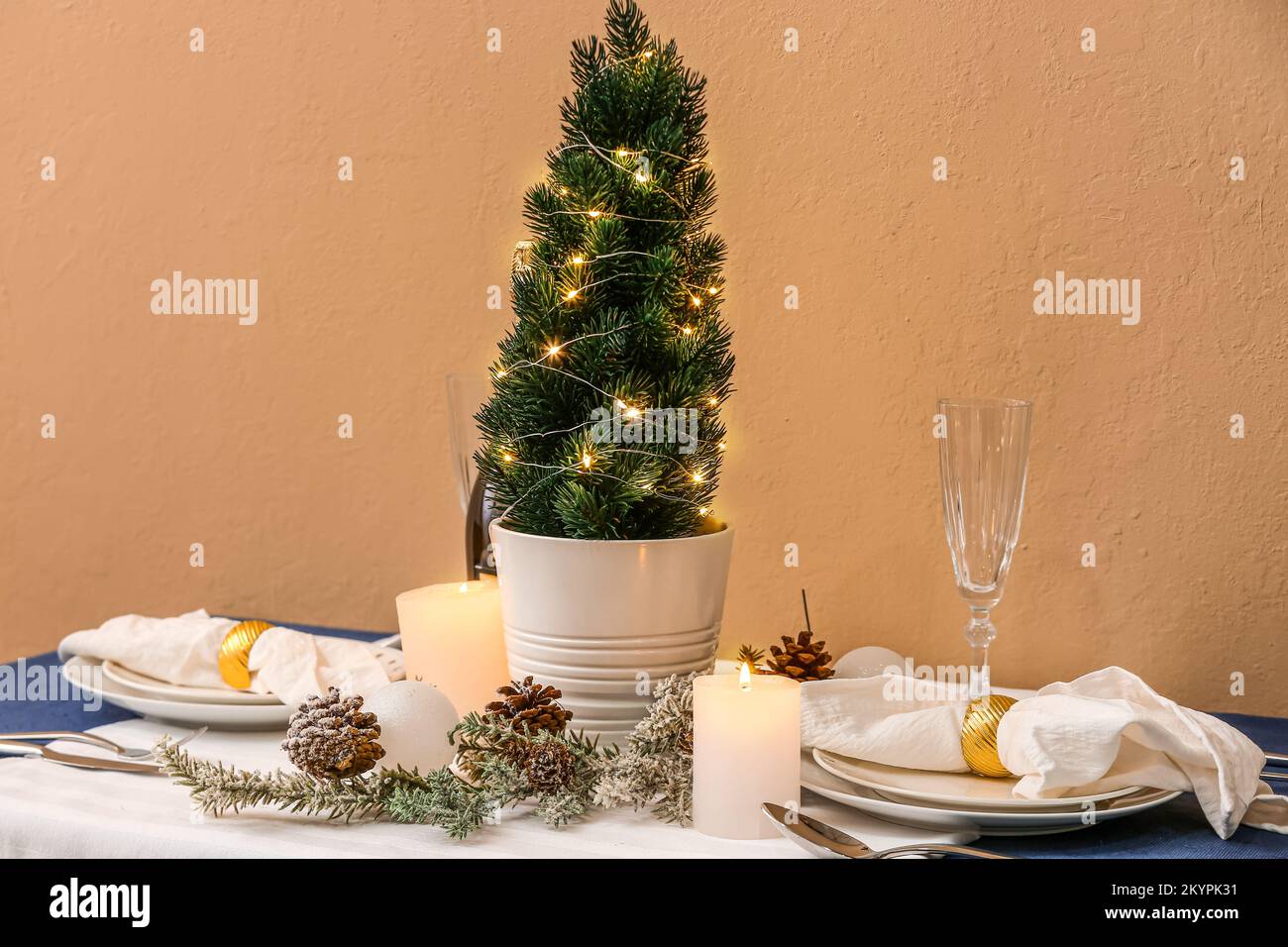 Table setting with small Christmas tree, fir cones and candles near ...