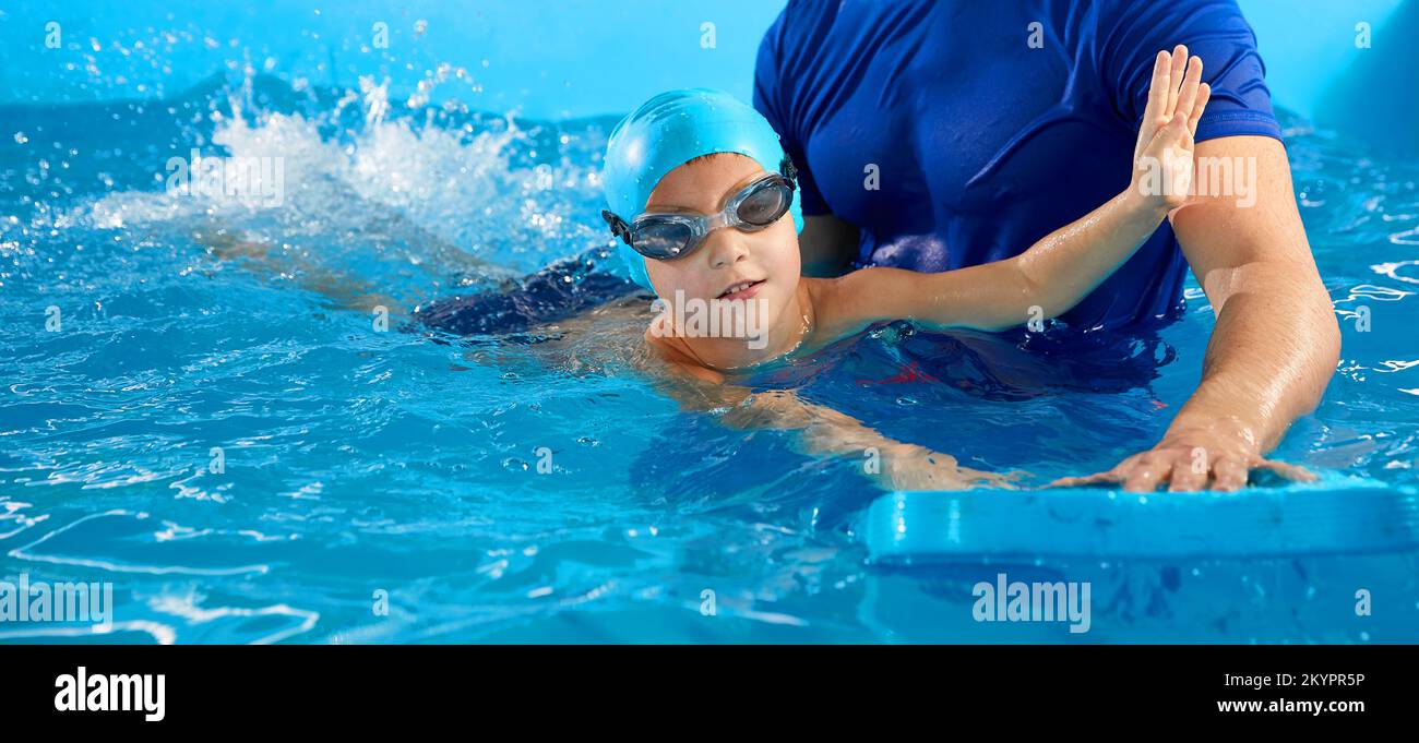Trainer teaching little boy how to swim in indoor pool with pool