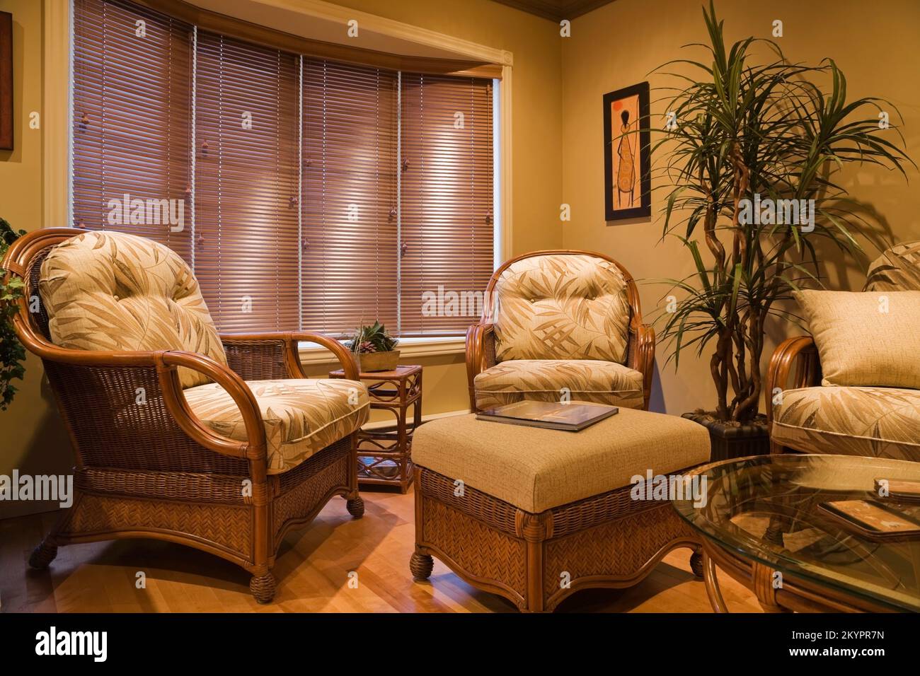 Wicker armchairs and glass top coffee table in living room inside small bungalow style home. Stock Photo