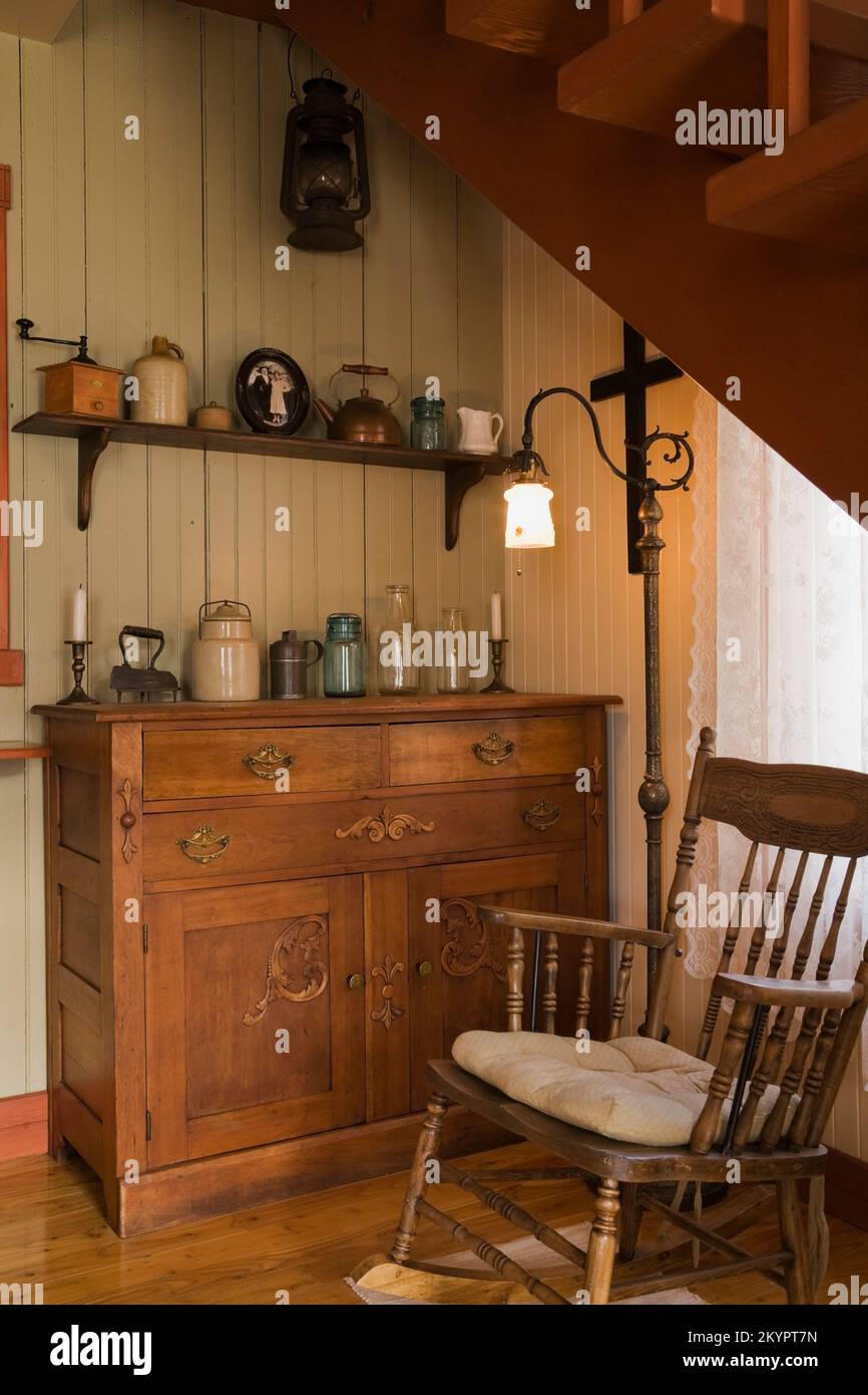 Antique rocking chair and dresser beneath stairs in dining room inside old circa 1825 Canadiana cottage style home. Stock Photo