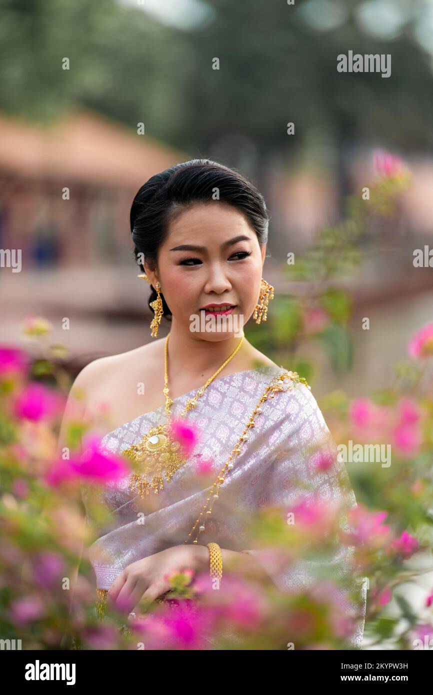 A woman in a traditional Thai costumes is standing on the wooden bridge while being taken a portrait photo shooting. Stock Photo