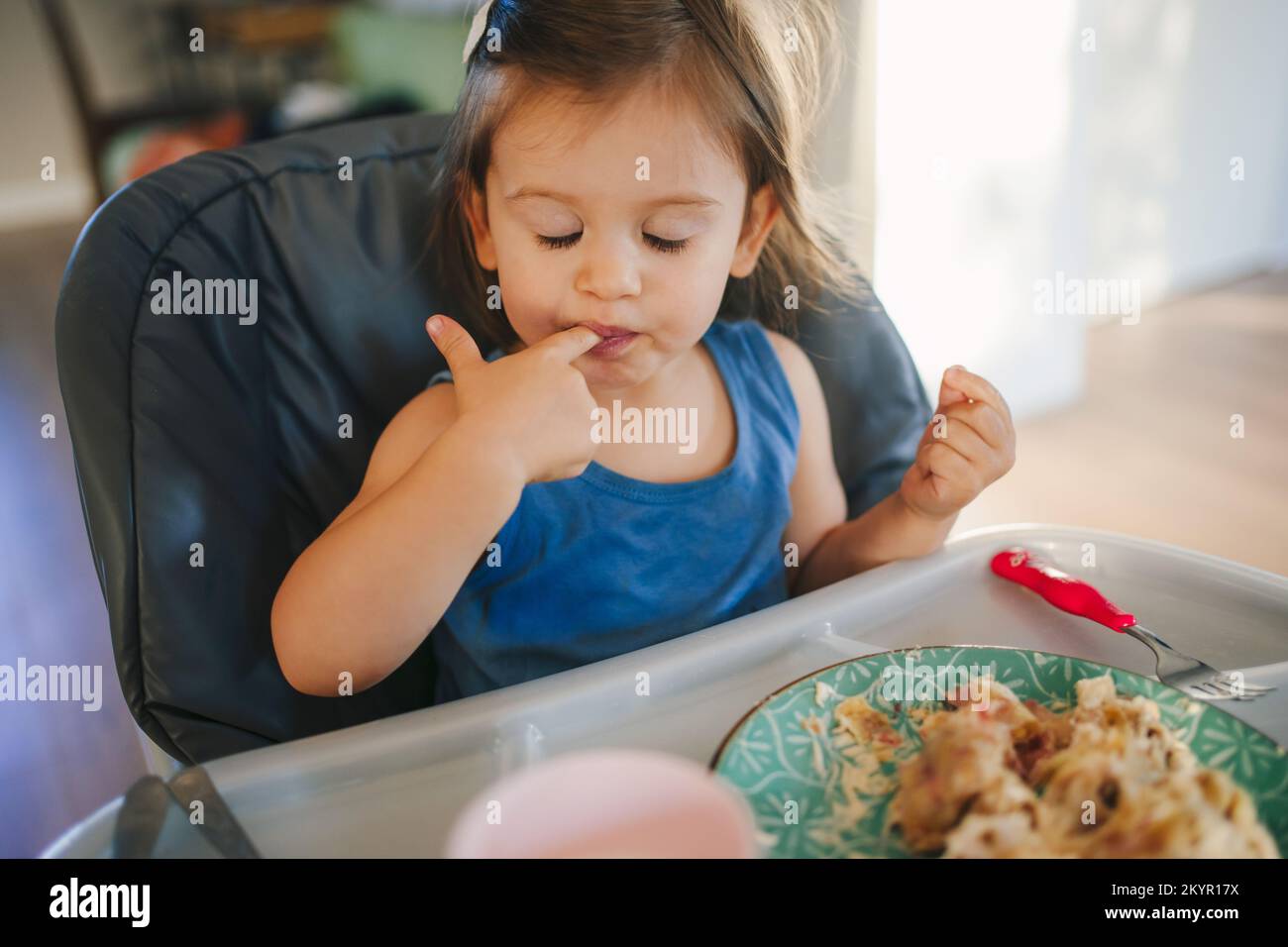 Adorable toddler baby girl sitting on high feeding chair eating homemade food at home. Children's closeup portrait. Healthy food. Healthy eating Stock Photo