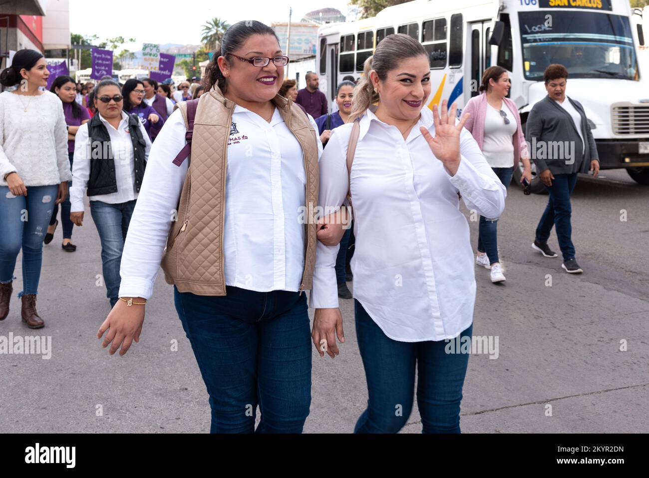 Two young females walking arm in arm in a march to protest violence against women stop to pose and wave, Guaymas, Mexico. Stock Photo