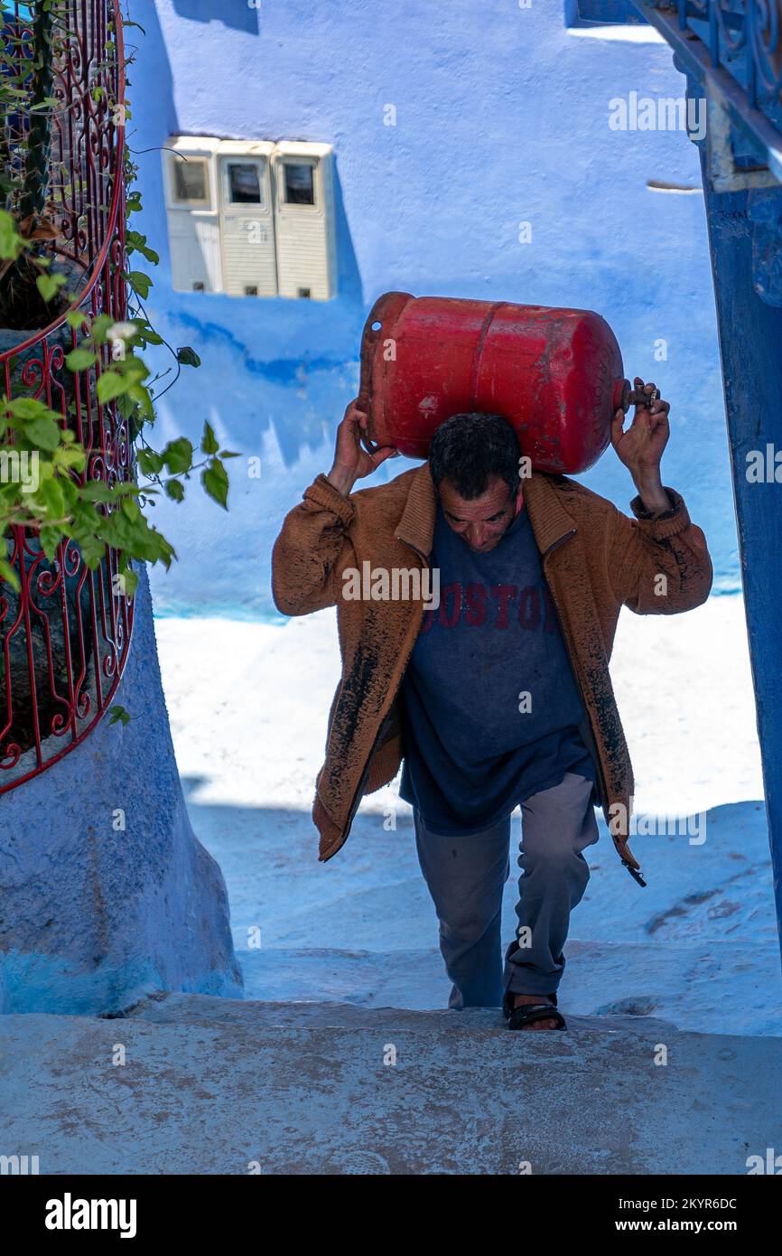 Carrying a red gas tank uphill in the 'Blue Town' of Chefchaouen, Morocco Stock Photo