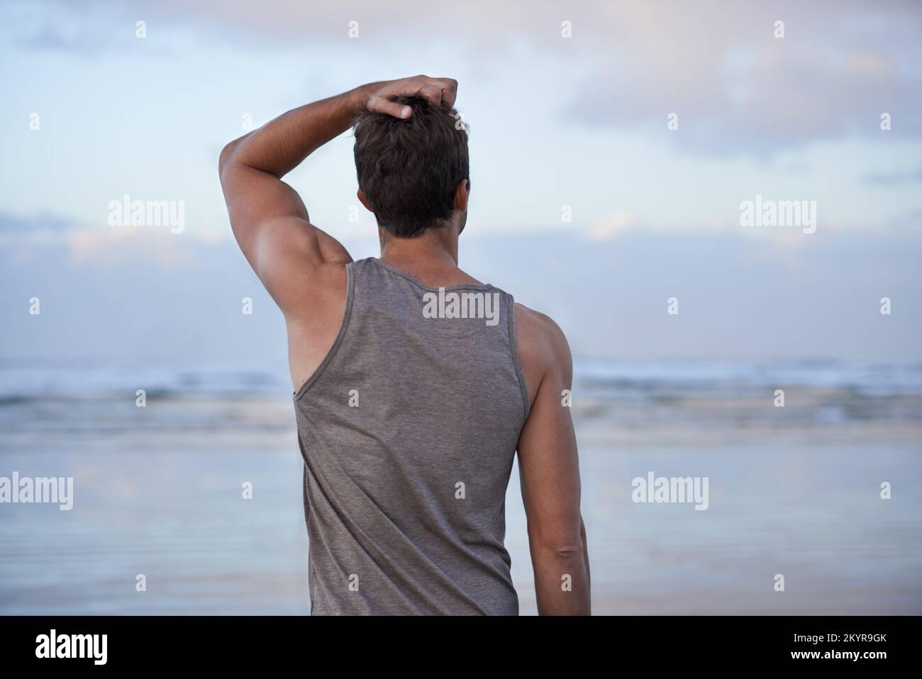 Contemplation on a beautiful morning. Rearview shot of a man with his hand in his hair looking out toward the ocean. Stock Photo