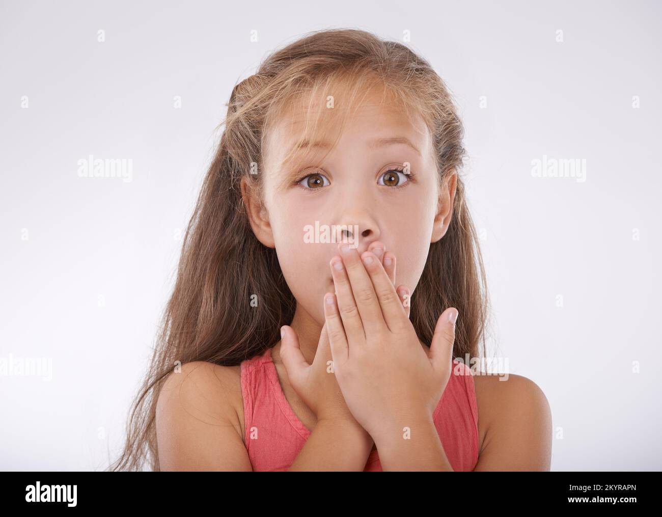 She cant believe it. Portrait of a little girl covering her mouth in disbelief. Stock Photo