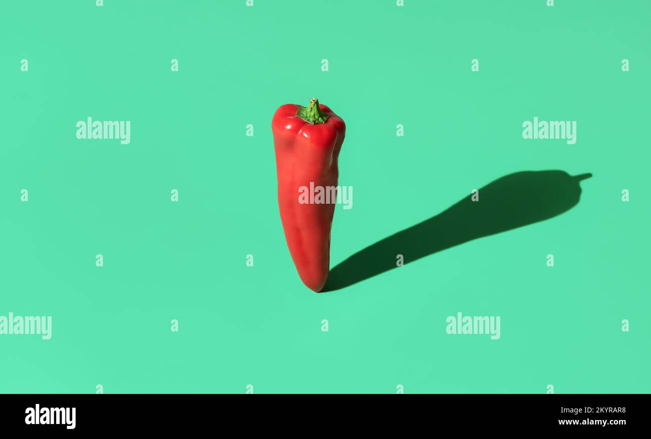 Single long red pepper minimalist on a green-colored table. Raw sweet pepper standing on a colorful background with a long strong shadow Stock Photo