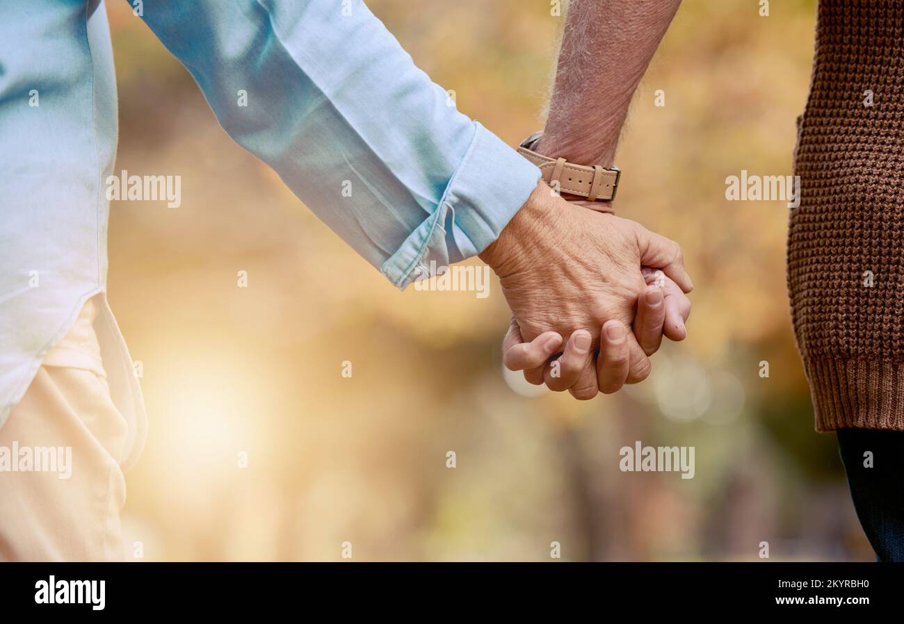 Love, nature and senior couple holding hands while walking in autumn park, forest or woods for retirement leisure. Romance, lens flare or marriage Stock Photo
