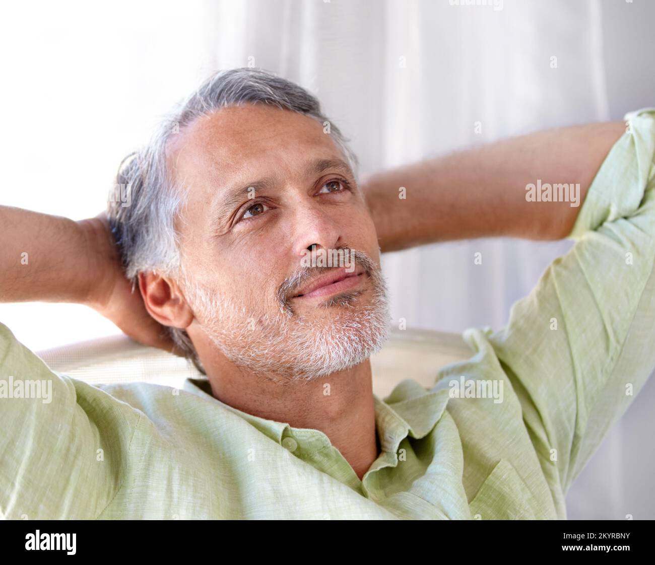 Laid-back. A mature man relaxing in his hone with his hands behind his ...
