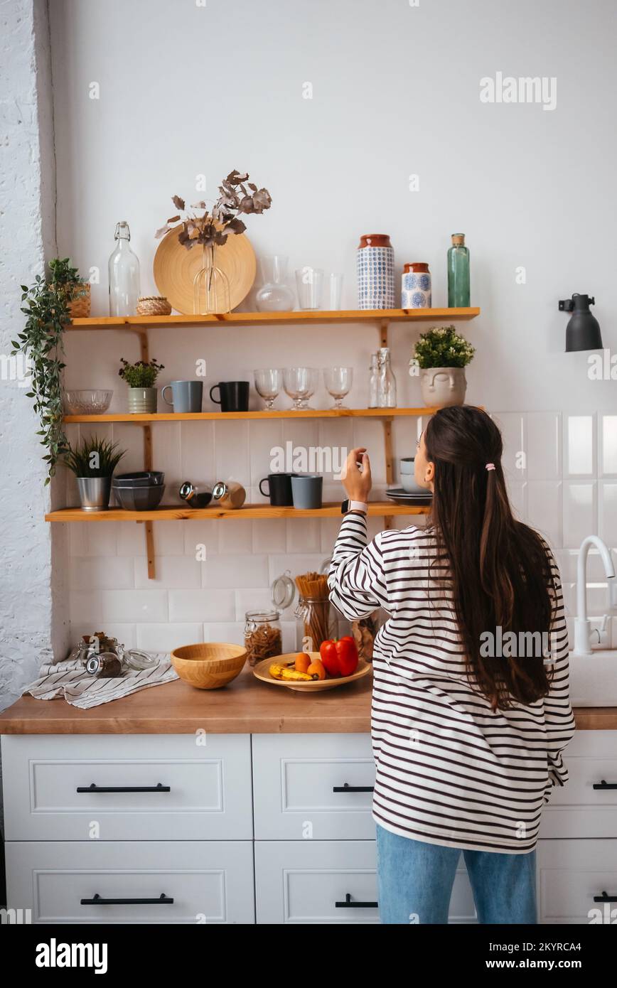 Woman takes out a glass from shelf in the kitchen Stock Photo