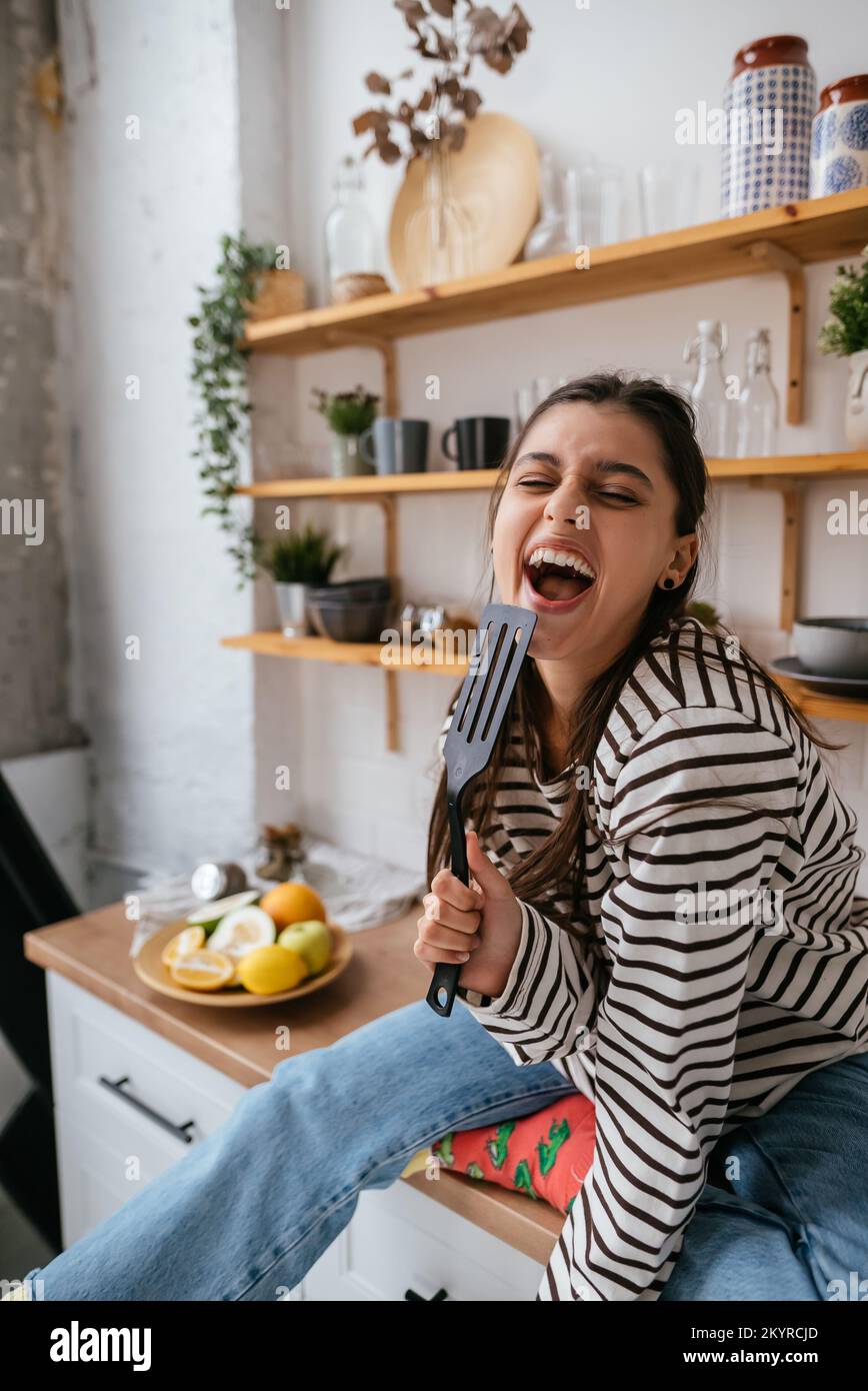 Funny woman singing into spatula, holding spatula as microphone. Stock Photo