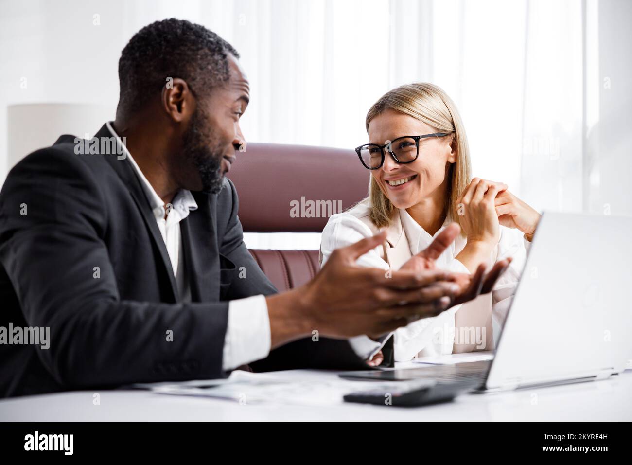 Two people analyze documents on a laptop while sitting at a table in the office. Business partners at work in the office are discussing projects Stock Photo