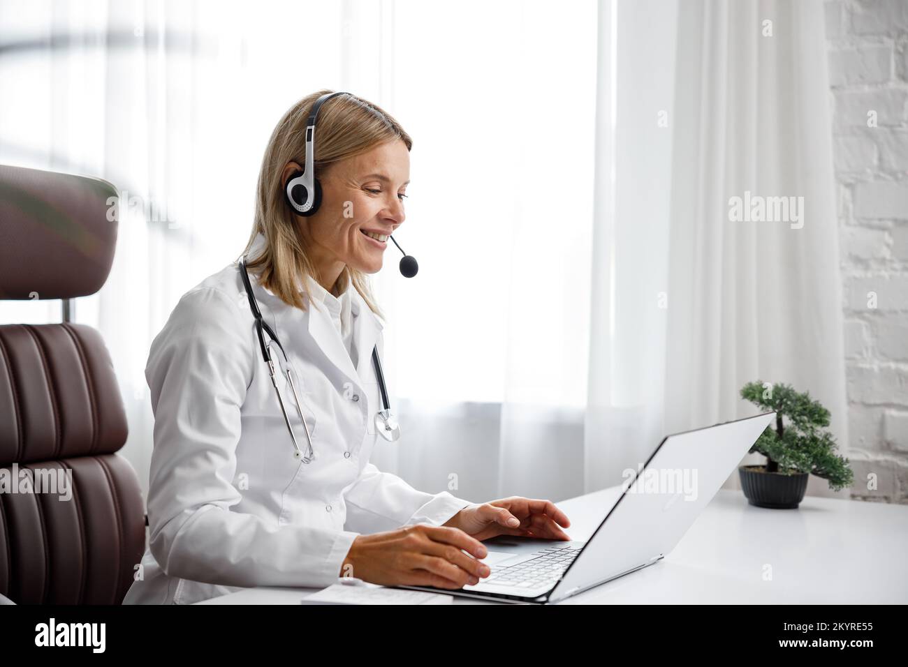 Telemedicine. Headshot portrait of smiling female doctor in headphones looking at camera. A female medical doctor remotely consults in a virtual Stock Photo